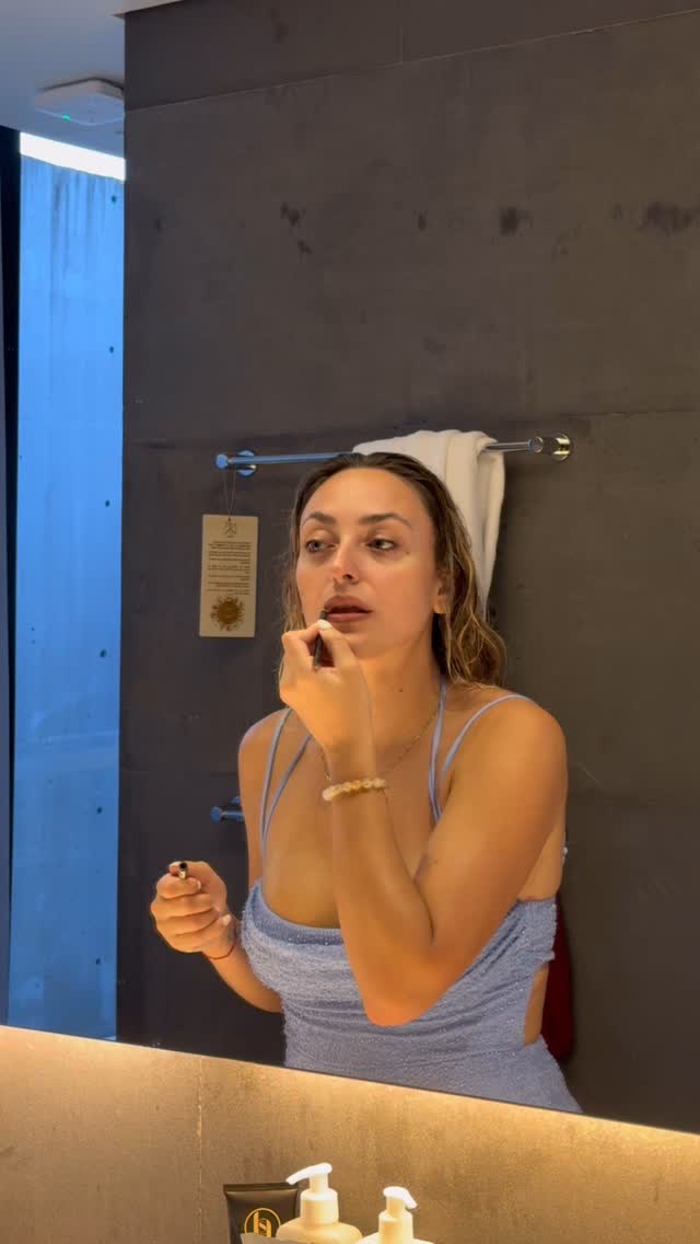 Sara doing her skincare in a bathroom mirror, hair wrapped in a towel.